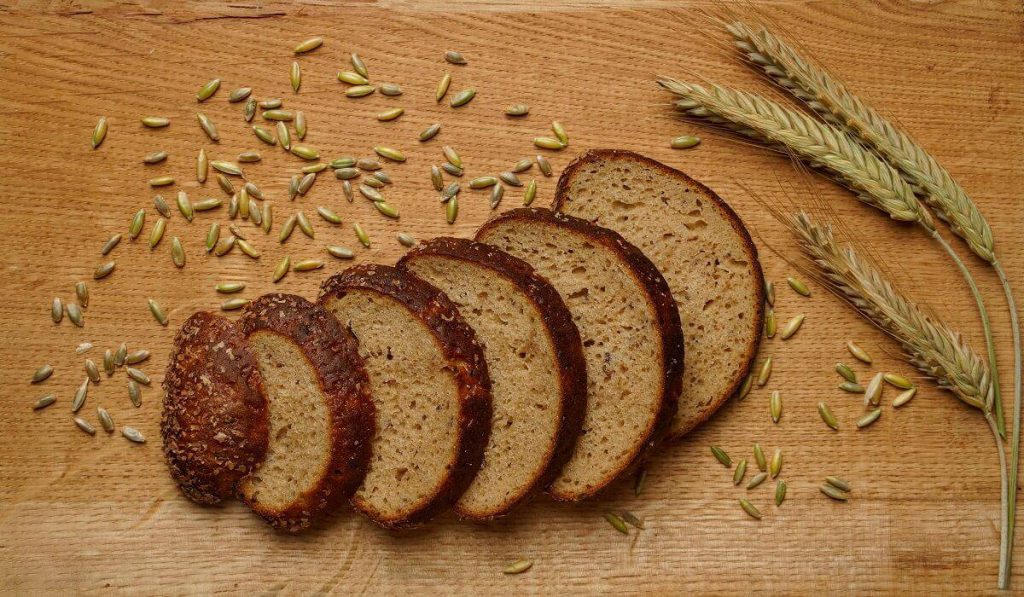 Slices of Brown Bread with scattered rye grains on a wooden board.