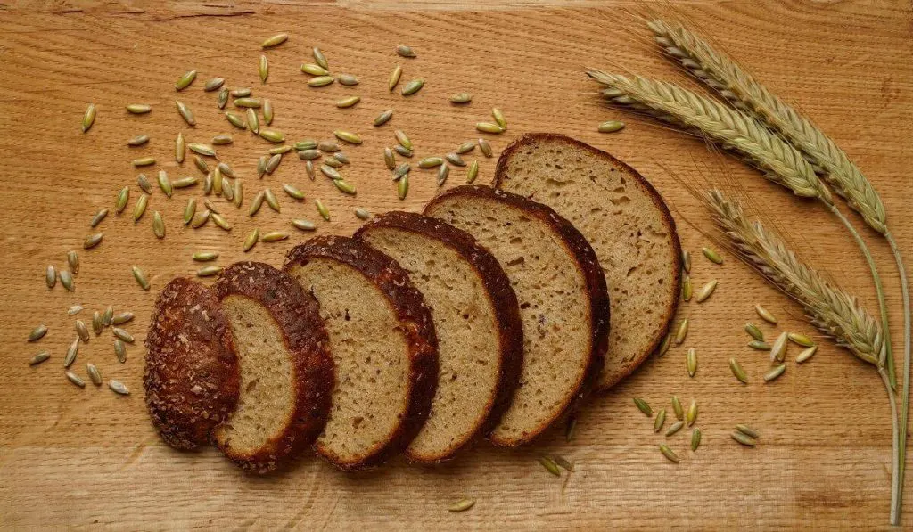 Slices of Brown Bread with scattered rye grains on a wooden board.