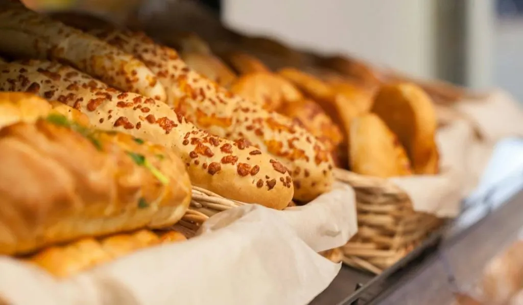 A shelf with baskets filled with different breads with herbs and cheese.