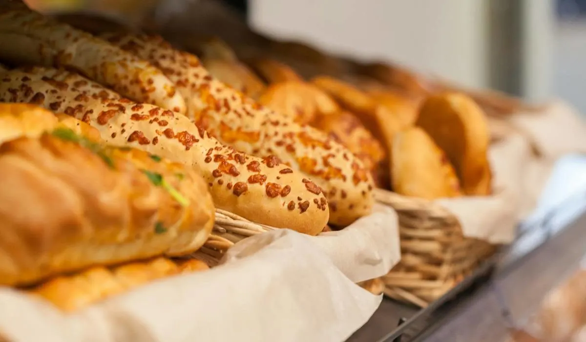 A shelf with baskets filled with different breads with herbs and cheese.