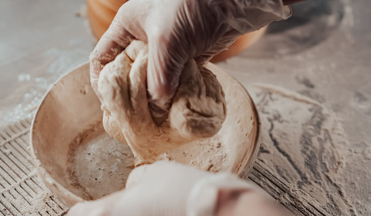 A persons hands with white gloves holding a mixture of flour and water.