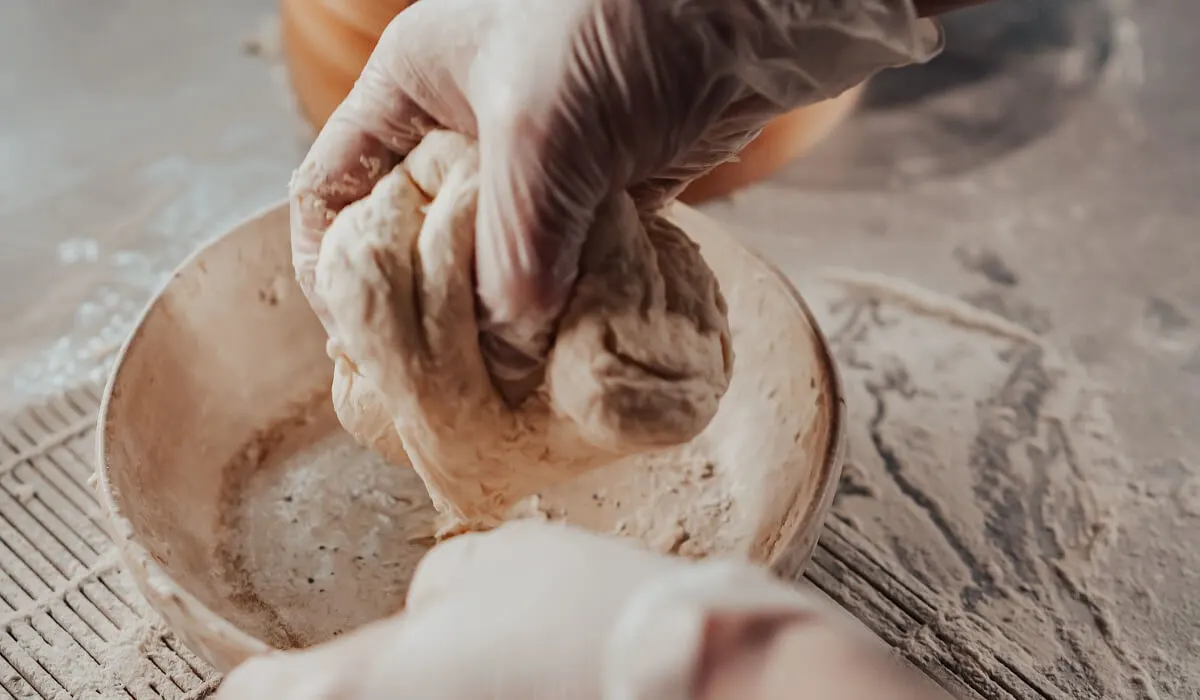 A persons hands with white gloves holding a mixture of flour and water.