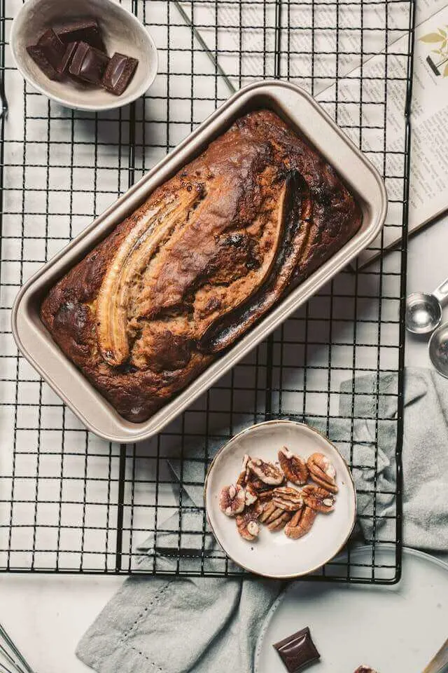 Banana bread in a tray with a chocolate and nuts beside it.