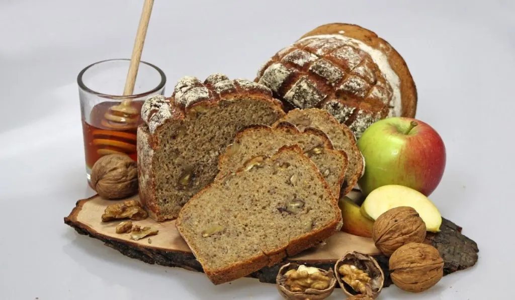 A bread on a wooden plate with honey, walnuts and apples decoration.