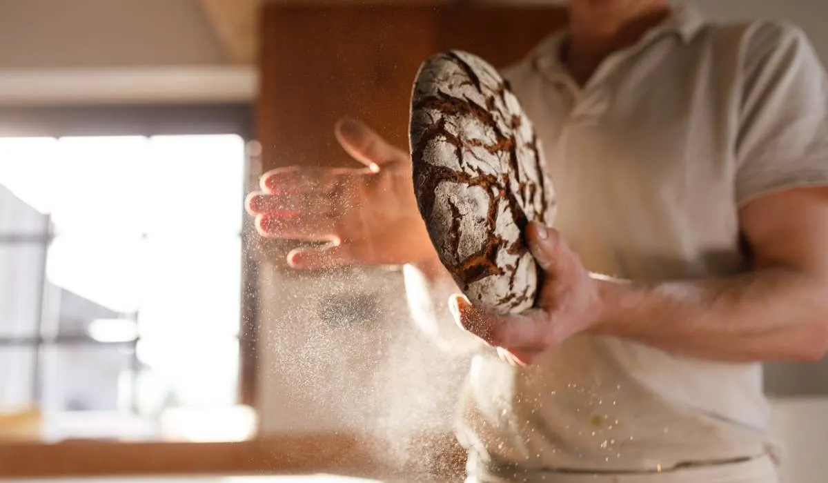 Man holding dark bread in his arms and sprinkles flour