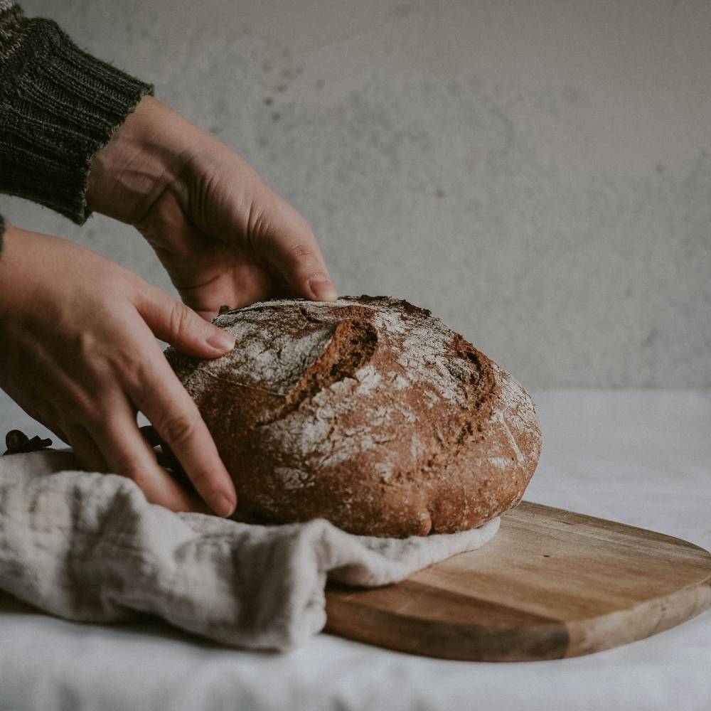 A person's arms putting sourdough bread on a wooden plate covered with cloth.
