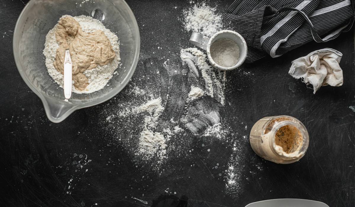 A cup filled with flour and sourdough starter in a jar beside it.