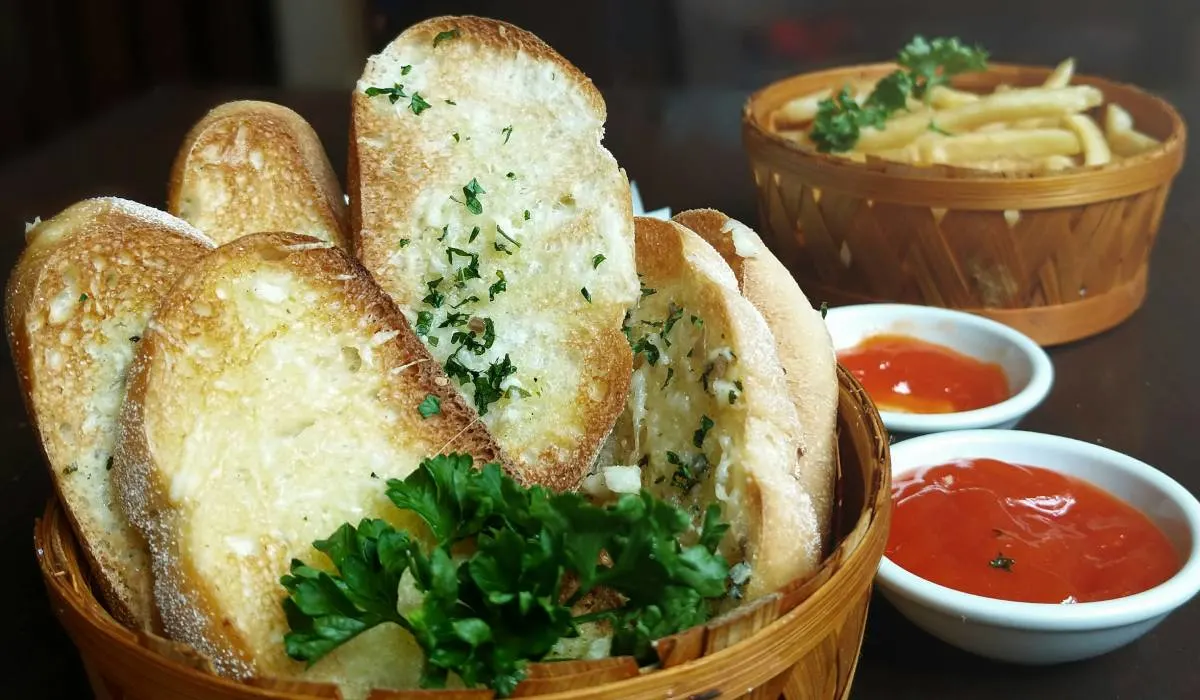 Sliced bread with Garlic in a Basket with tomato sauce and french fries in the background