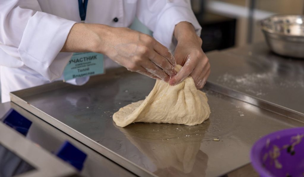 A person kneading dough and doing windowpane test